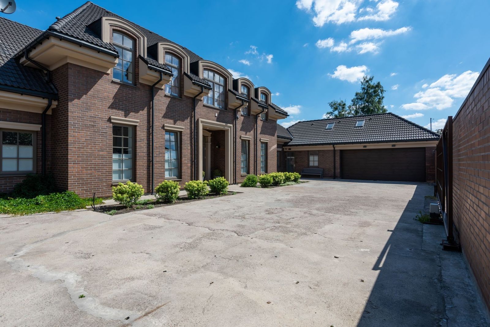 Elegant brick house exterior with a large driveway under a clear blue sky.