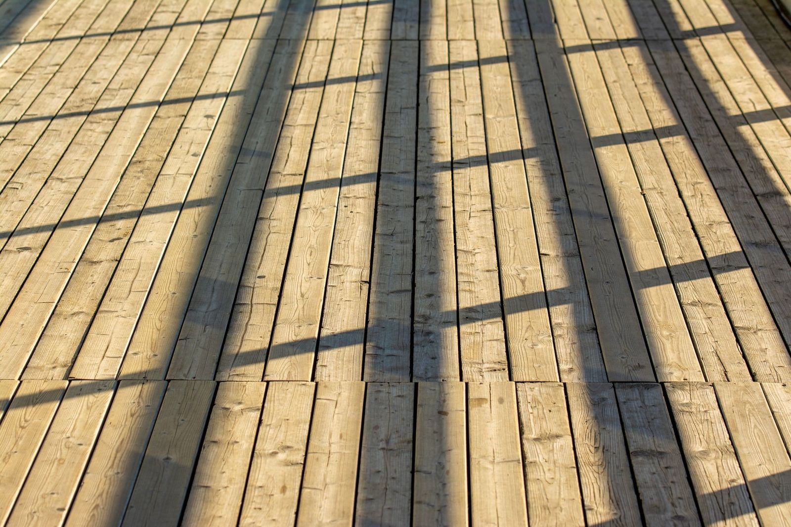 A wooden deck beautifully lit by sunlight, casting geometric shadows of a railing.